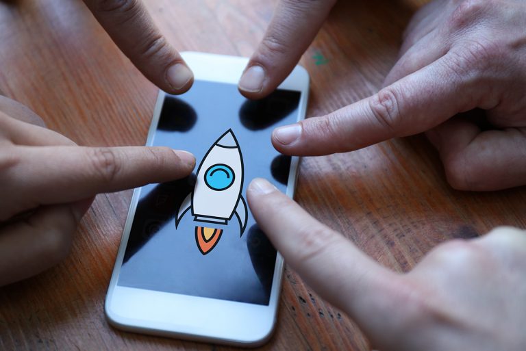 Rocket ship illustration on mobile phone, with fingers pointing at it.